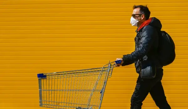 Man with a shopping cart in front of a store wearing a mask